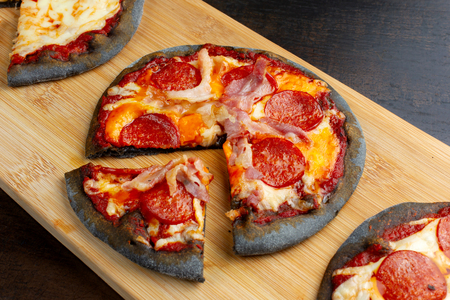 Creative pizza on black dough, three pieces on the board.の写真素材