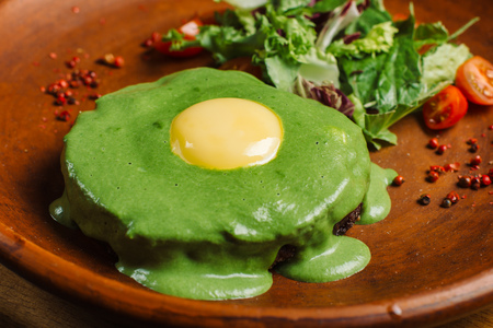 Meat with green sauce with egg on a clay plate.の写真素材
