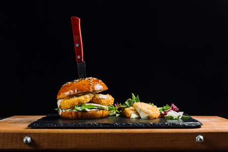 Hamburger with cheese sticks laid out on a black slate. Cheese beautifully flows.の写真素材