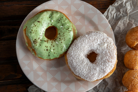 Two donuts, one with green icing, the second is sprinkled with coconut chips. Lie on a beautiful plate. Wooden table, Kraft paper. Top view.の写真素材