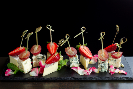 Cheese plates served with strawberry and grapes on black slate.の写真素材