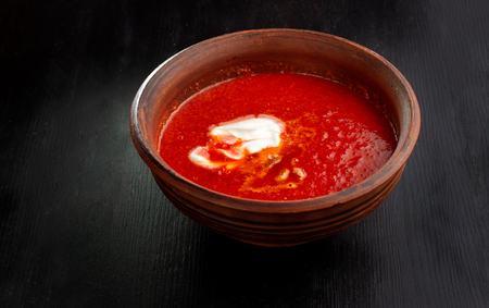 Tomato soup, handmade clay plate on a black background.の写真素材
