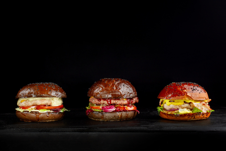 Set of three delicious burgers isolated on a dark background. The concept of fast food, delicious but unwholesome food.の写真素材