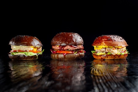 Set of three delicious burgers isolated on a dark background. The concept of fast food, delicious but unwholesome food.の写真素材