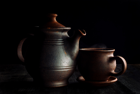 Tea cup and teapot, on a wooden table, beautiful sunshine and black background.の写真素材