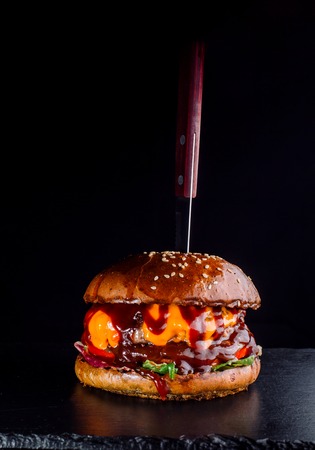 A burger on the black background with a sticking knife.の写真素材