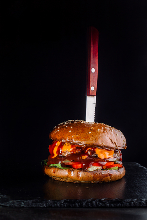 A burger on the black background with a sticking knife-2.の写真素材