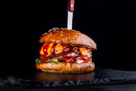 A burger on the black background with a sticking knife.の写真素材