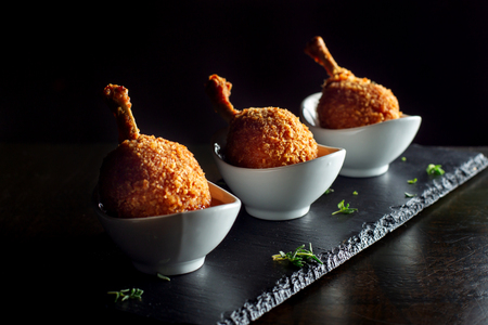 Three breaded chicken legs in sauceboats, stand on black slate.の写真素材
