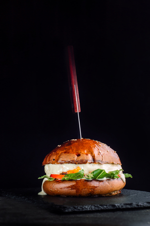 A burger on the black background with a sticking knife.の写真素材