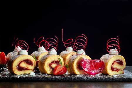 Homemade cake roll with strawberry cream a on a black slate.の写真素材