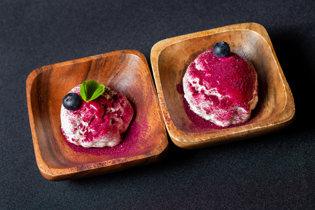 Wooden plate of blueberry ice cream with fresh berries on black table.の写真素材