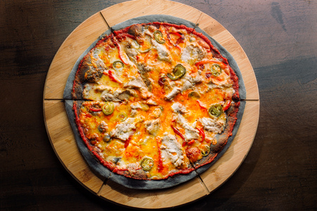 Pizza with jalapeno pepper, dried tomatoes and chicken breast on black dough.の写真素材