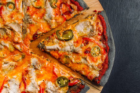 Pizza with jalapeno pepper, dried tomatoes and chicken breast on black dough.の写真素材