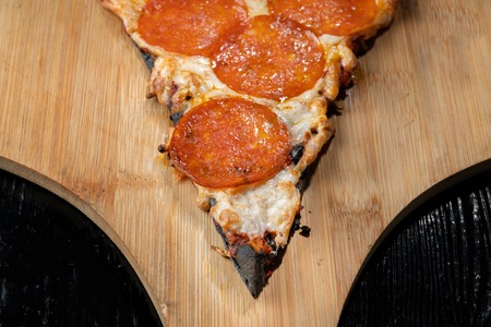 A slice of margarita pizza, on black dough. Lies on a wooden platform.の写真素材