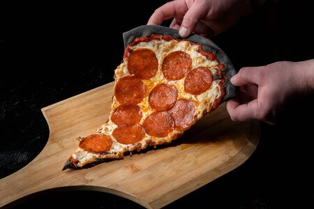 A slice of pepperoni pizza, on black dough. Lies on a wooden platform.の写真素材