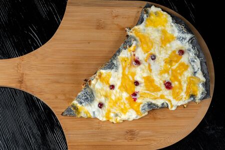 A slice of pizza with cranberries from black dough lying on a wooden board.の写真素材