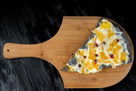 A slice of pizza with cranberries from black dough lying on a wooden board.の写真素材