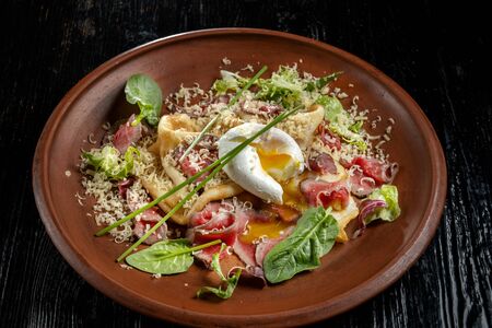 Diet menu. Salad with chopped steak, poached eggs, pancakes, green salad. Sprinkled with grated cheese. Side view. The yolk is clearly visibleの写真素材