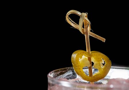 Bamboo skewer with pickled jalapenos in a cocktail.