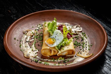 Rolled pancakes on top lies scrambled eggs. Beautiful clay plate. Shooting from the end of pancakes.の写真素材