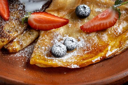 Pancakes with ice cream, with blueberries and strawberries, sprinkled with icing sugar. Focus on blueberries, macro.の写真素材
