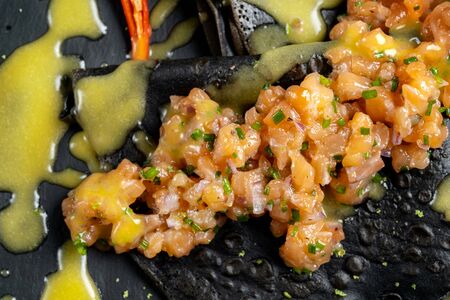 Black dough pancakes with tartar and sauce. Nearby lies a grilled lemon and chili pepper.