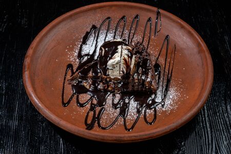 Chocolate brownie with vanilla ice-cream and chocolate sauce is laid out on a clay plate.の写真素材