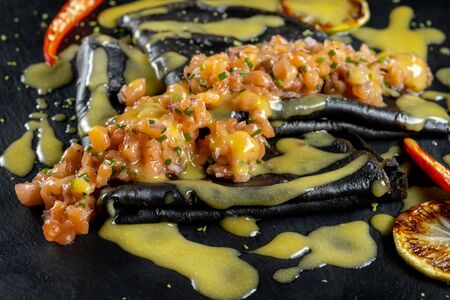 Black dough pancakes with tartar and sauce. Nearby lies a grilled lemon and chili pepper.の写真素材