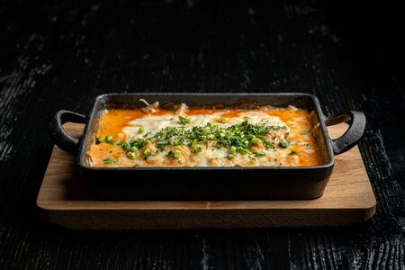 Cooked hot lasagna, in a beautiful cast-iron bowl. Side view.