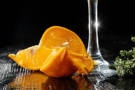 Orange slices lie near the thin legs of the glass. Black table, back light.の写真素材