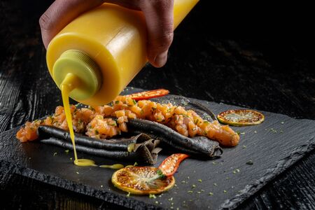 Black dough pancakes with tartar and sauce. Nearby lies a grilled lemon and chili pepper.の写真素材