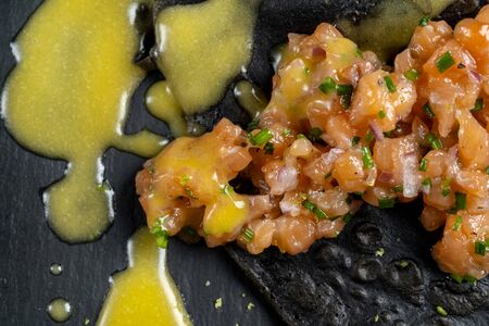 Black dough pancakes with tartar and sauce. Nearby lies a grilled lemon and chili pepper.の写真素材