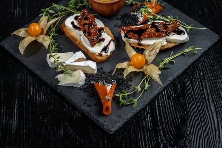 Snacks are laid out on black slate, physalis, salami, cheese and sun-dried tomatoes.の写真素材