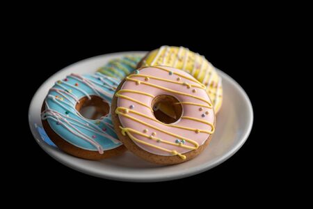 Four gingerbreads in the form of a donuts lie on a white glass plate on a black isolated background.の写真素材