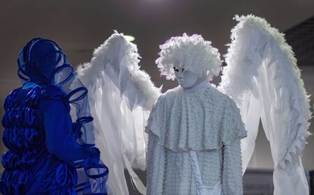 Wearing costume, large white wings, white mask, with long white drapery.