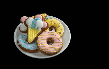 Four gingerbreads in the form of a donuts lie on a white glass plate on a black isolated background. Gifts for the New Year.の写真素材