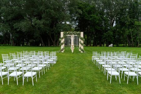 Outdoor wedding of a park. Wedding arch on the field, chiavari chairs are on display.の写真素材
