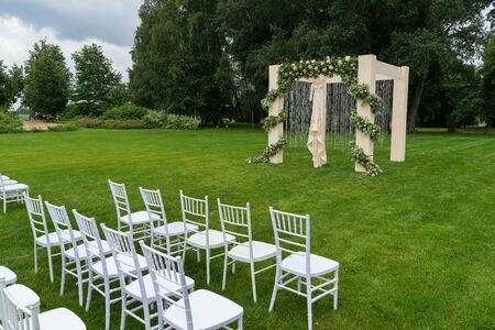 Outdoor wedding of a park. Wedding arch on the field, chiavari chairs are on display. Side view.の写真素材