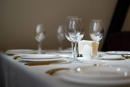 Chic and elegant, gold-plated cutlery and white plates, table setting with empty plates. Glasses in the light from the window. Side view.の写真素材