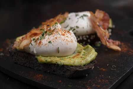 Poached eggs with bacon on toasts. Black bread toast with sesame seeds. Macro.の写真素材