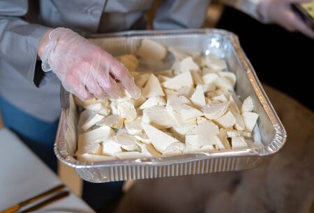 An aluminum tray in the hands of a cook with sliced pieces of cheese.の写真素材