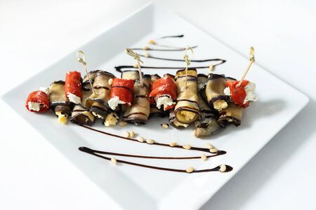 Eggplant rolls stuffed with cottage cheese, lie on a plate decorated with sauce with pine nuts.の写真素材