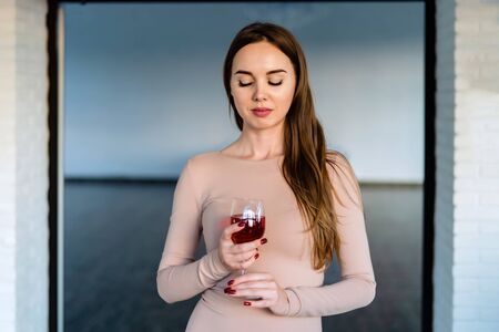 Beautiful young woman in pink dress holding a glass of red wine in her hands.の写真素材