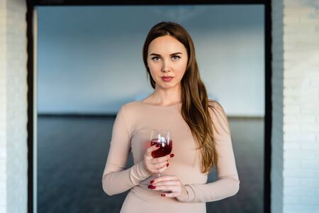 Beautiful young woman in pink dress holding a glass of red wine in her hands.の写真素材