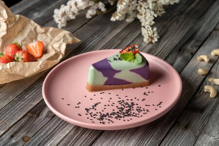 Blueberry cake, lemon, mint. Vegan, lactose free and sugar free. Laid on a pink plate, decorated with strawberries and sprinkled with black sesame seeds. On a wooden background in rustic style.の写真素材
