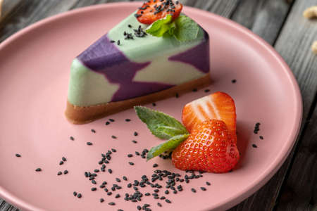 Cut strawberries on a pink plate, sprinkled with black sesame seeds. In the background is a vegan cake. Strawberry Focus. Clouse-up.の写真素材
