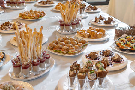 Luxury catering, a snack table, bread sticks, desserts, rolls. Mini chicken burgers with cheese and tomatoes on a white plate-2.の写真素材