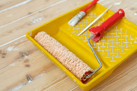 Yellow painting tray cuvette and paint roller with red handle, made of synthetic fiber.