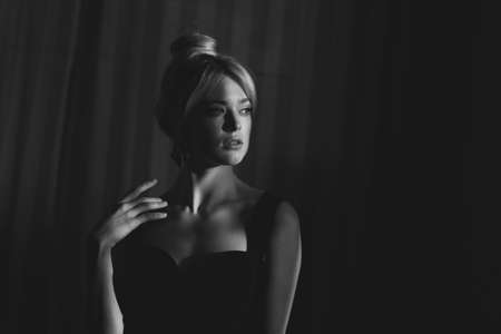 Close up studio portrait of a pretty blonde woman in black top. A face in a beautiful sun glare.の写真素材